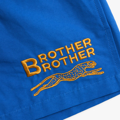Brother Brother Nylon Baggie. Close-up of lapis blue shorts showing orange Brother Brother graphic and stitched hem.