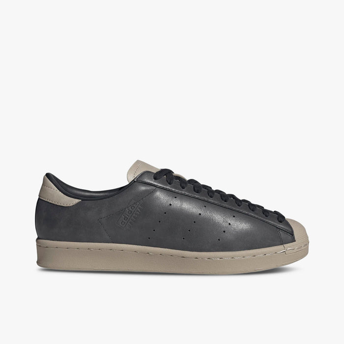 adidas Superstar Vintage Short Shell. Side view of Carbon leather sneakers with perforated three-stripes, adidas Superstar debossing on the sidewall, and Wonder Beige midsole.